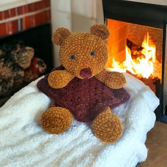 Handmade crochet bear lovey sitting on a white fluffy blanket in front of a glowing fireplace — Dave the Anti-Anxiety Bear by Nana's Attic Crochet
