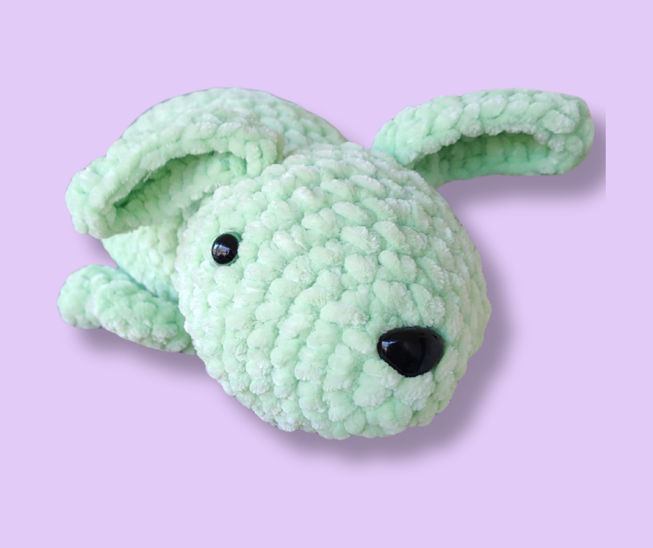 Handmade green crochet plush bunny made with soft plush yarn, shown on a light lavender background.