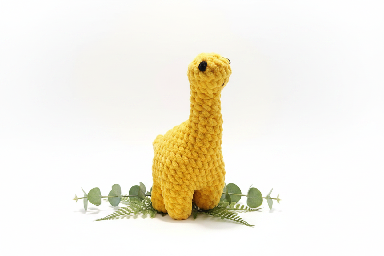 Yellow crochet plush Brontosaurus on white background with greenery